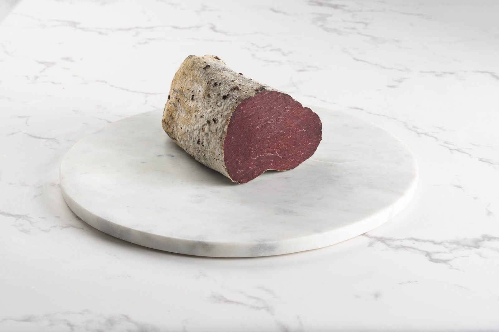Un pezzo di brisaola stagionata, con la crosta di spezie, su un piatto di marmo