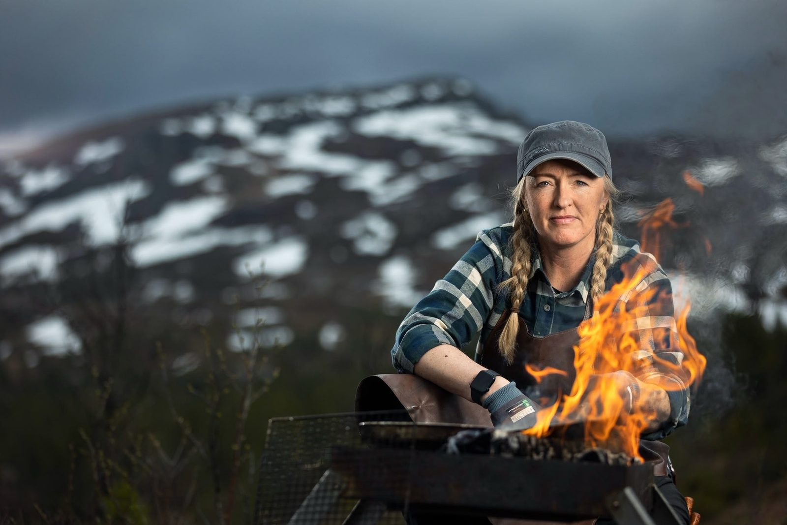Lena Flaten accanto al fuoco, con le montagne innevate alle spalle